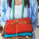 Cropped image of smiling seamstress holding stack of colored fabric